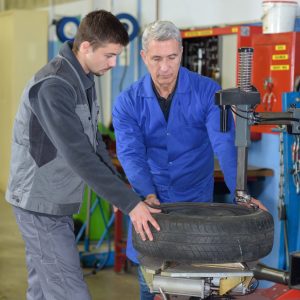 Apprentice mechanic and teacher retreading wheel in automotive centre