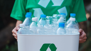 Bin of empty plastic bottles being carried by person wearing a recycling t-shirt